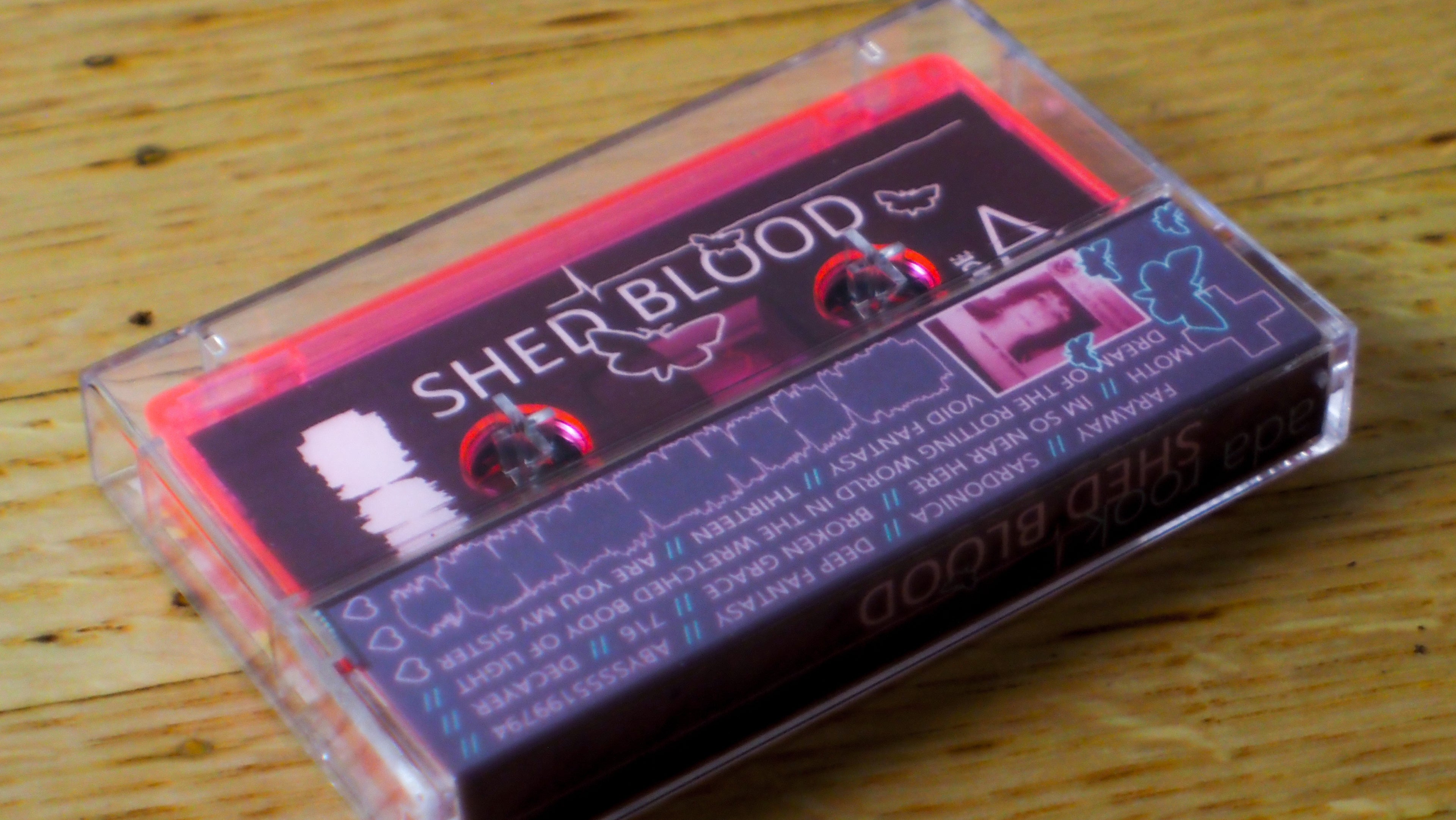 Cassette tape with 'SHED BLOOD' branding on a wooden surface