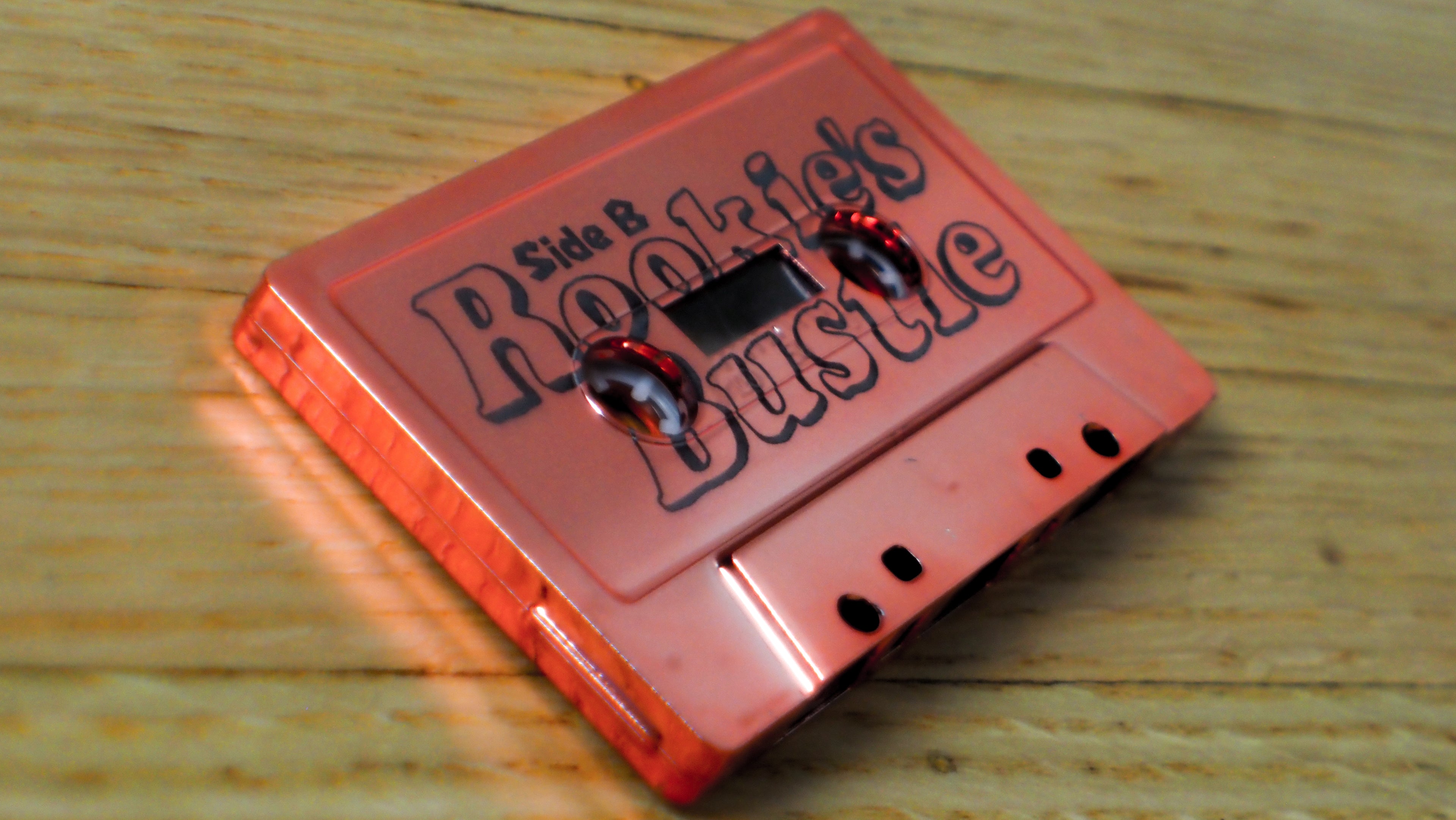 Red cassette tape with 'Rookie's Bustle' text on a wooden surface