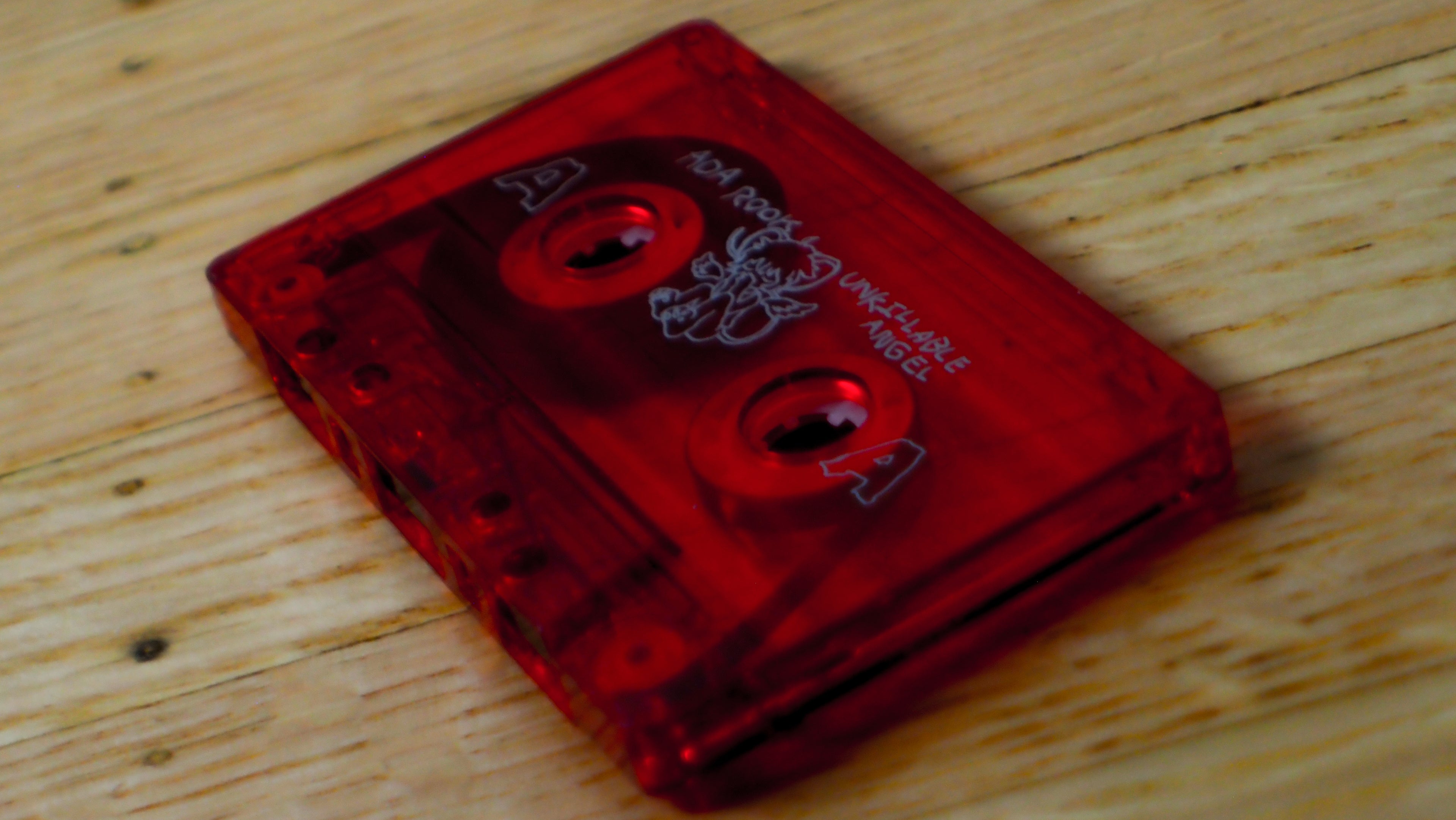 Red cassette tape for "Unkillable Angel" on a wooden surface