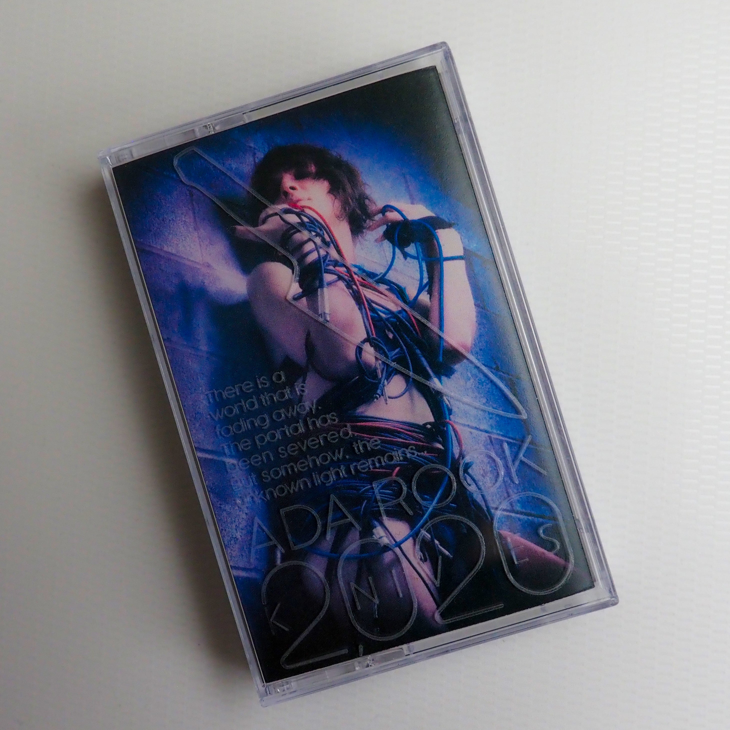 Cassette tape case art for 2020 Knives, featuring Ada Rook covered in wires on a brick wall background