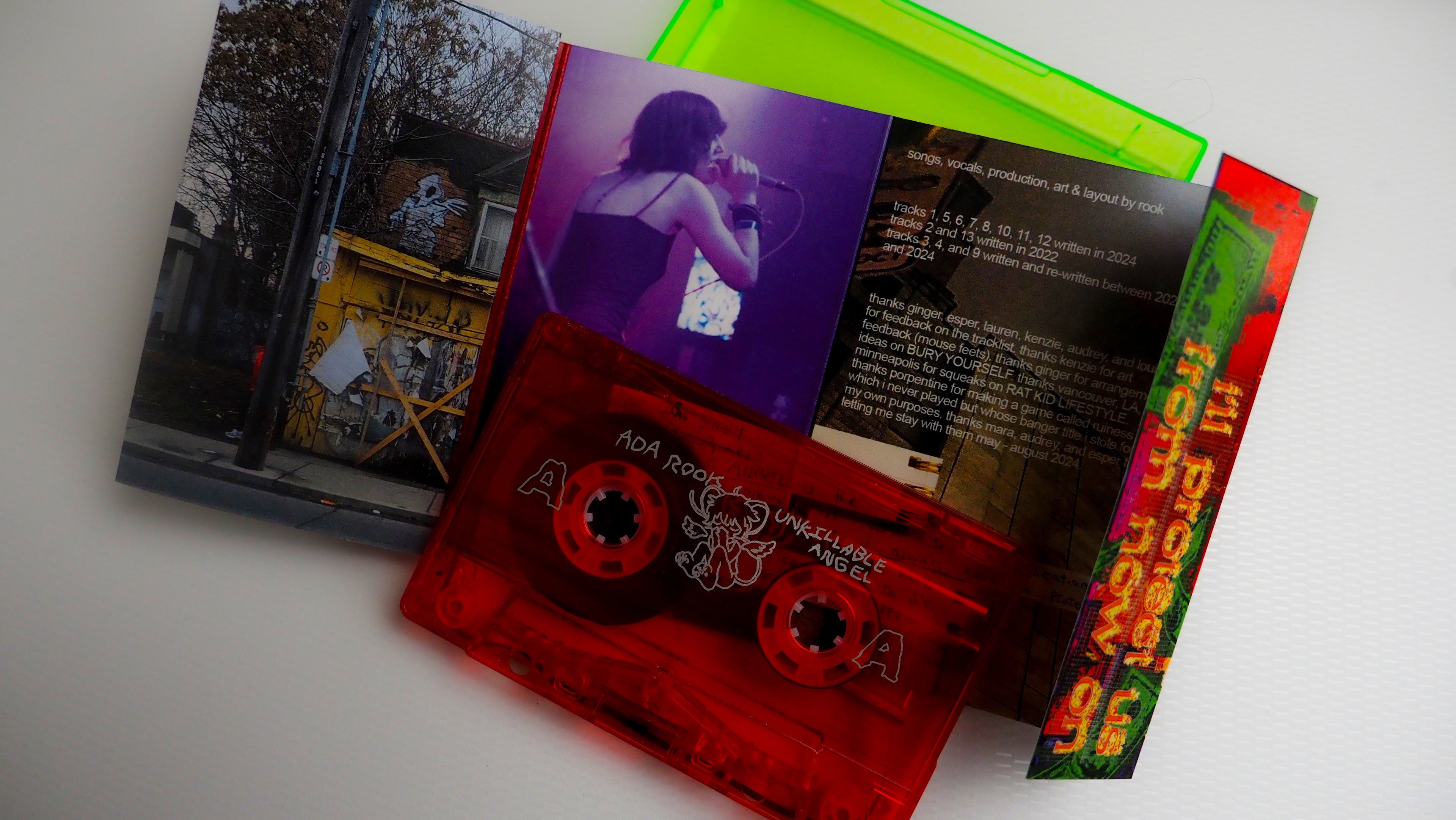 Red and flourescent green-colored cassette tape and booklet for Unkillable Angel on a white background.